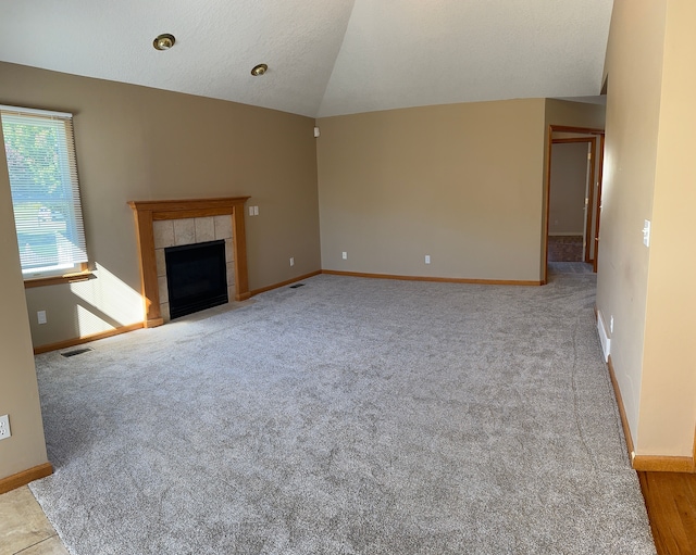 unfurnished living room featuring light colored carpet, a textured ceiling, a tile fireplace, and vaulted ceiling