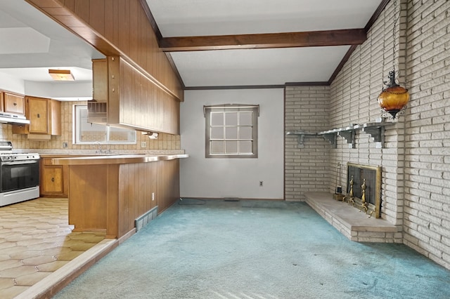 kitchen featuring lofted ceiling with beams, light carpet, a brick fireplace, stainless steel range with gas cooktop, and kitchen peninsula