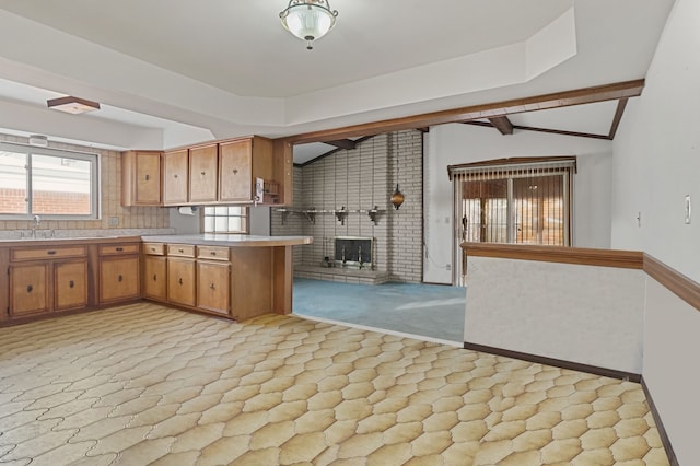 kitchen featuring sink, vaulted ceiling with beams, kitchen peninsula, a brick fireplace, and light carpet