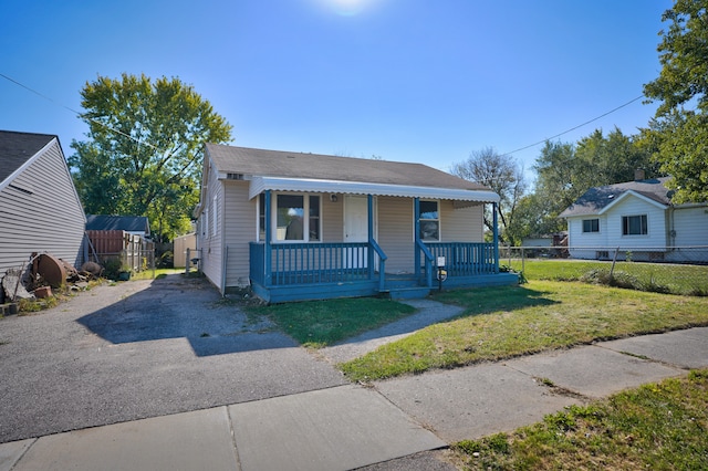 bungalow with driveway, covered porch, a front lawn, and fence