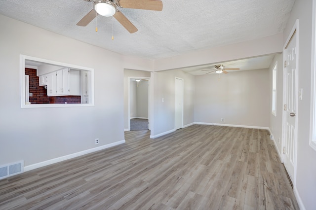 unfurnished room with light wood finished floors, visible vents, a textured ceiling, and baseboards