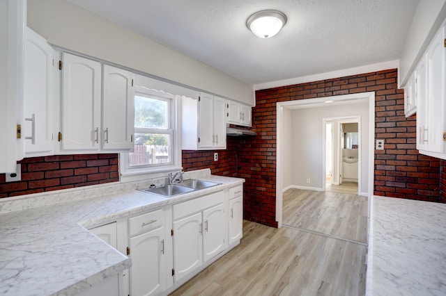 kitchen with light wood-style flooring, a sink, under cabinet range hood, white cabinets, and light countertops