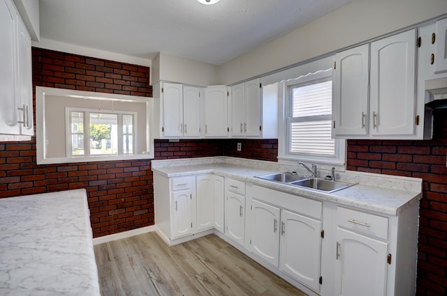 kitchen featuring a sink, light wood-style floors, brick wall, and white cabinetry