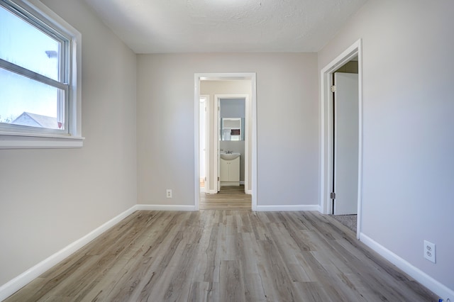 unfurnished bedroom featuring a sink, baseboards, a textured ceiling, and light wood finished floors