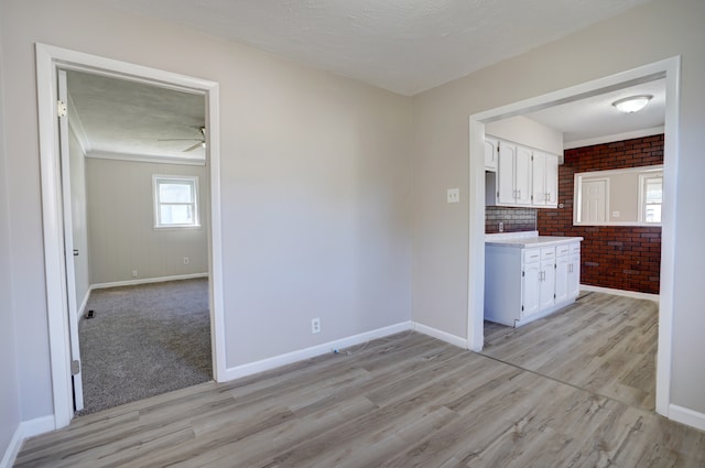 interior space featuring light wood-style flooring, brick wall, and baseboards