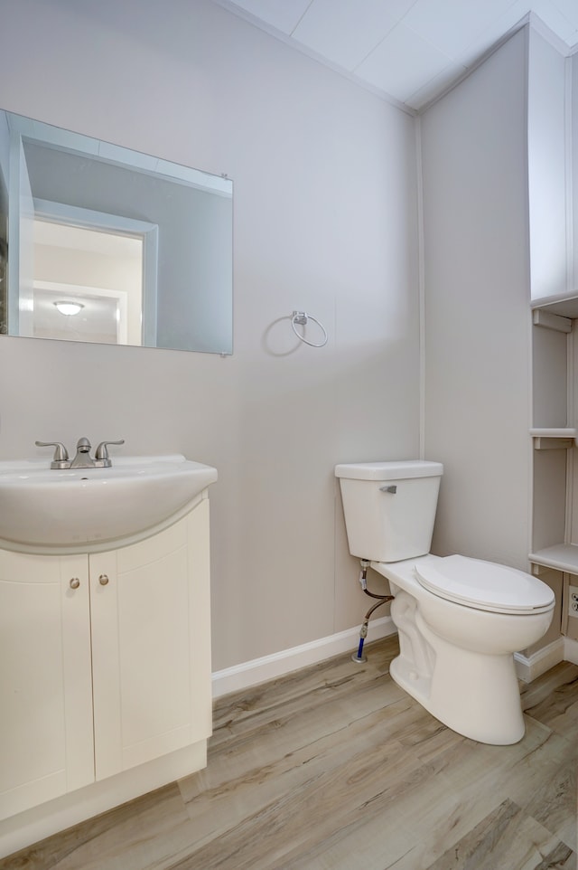 half bath with vanity, toilet, wood finished floors, and baseboards