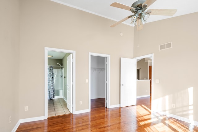 unfurnished bedroom featuring a spacious closet, ceiling fan, a high ceiling, ensuite bathroom, and light hardwood / wood-style floors