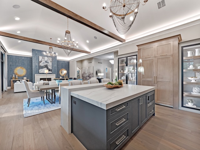 kitchen featuring lofted ceiling with beams, hanging light fixtures, light hardwood / wood-style flooring, a kitchen island, and light stone counters