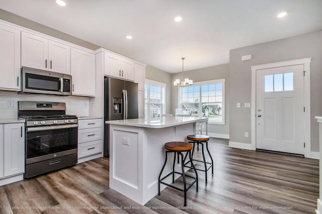 kitchen with white cabinets, appliances with stainless steel finishes, a kitchen island, and hanging light fixtures