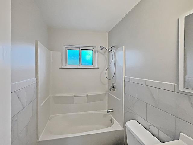 bathroom featuring shower / bathtub combination, toilet, and tile walls