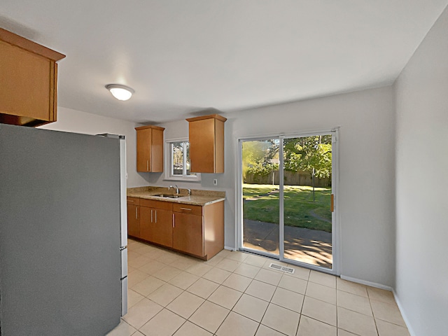 kitchen with light tile patterned flooring, stainless steel refrigerator, and sink