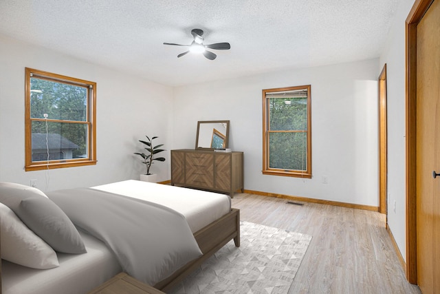 bedroom with a textured ceiling, ceiling fan, and light wood-type flooring