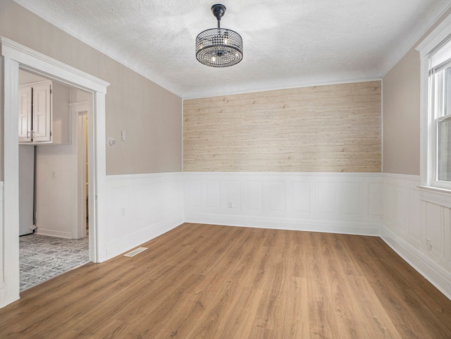 spare room with an inviting chandelier, a textured ceiling, wooden walls, and light hardwood / wood-style flooring