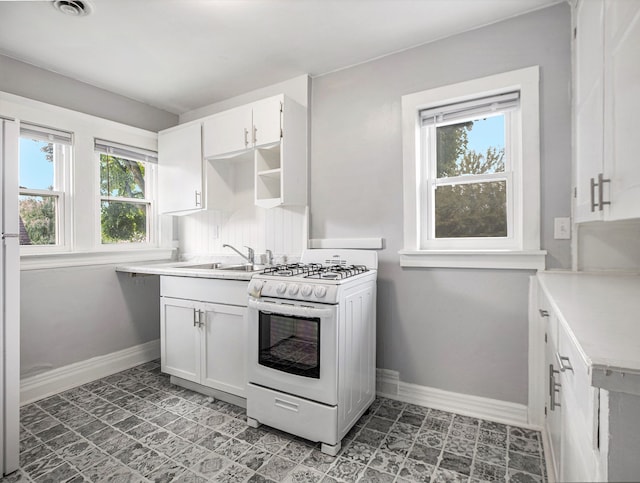 kitchen featuring a wealth of natural light, white cabinetry, white gas range, and sink