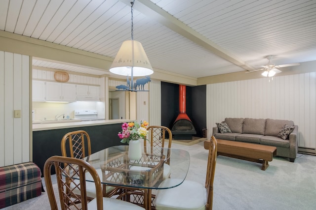 carpeted dining area featuring beamed ceiling, baseboard heating, a wood stove, and ceiling fan