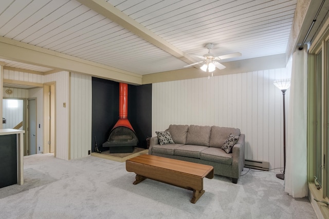 living room with beam ceiling, light colored carpet, a wood stove, and a baseboard radiator