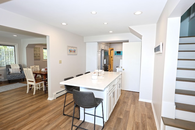 kitchen with stainless steel refrigerator with ice dispenser, a baseboard heating unit, light hardwood / wood-style floors, a breakfast bar, and white cabinets