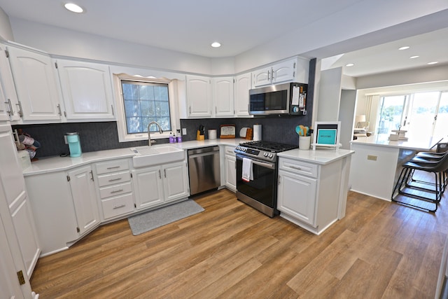 kitchen with stainless steel appliances, kitchen peninsula, a breakfast bar, white cabinets, and light wood-type flooring