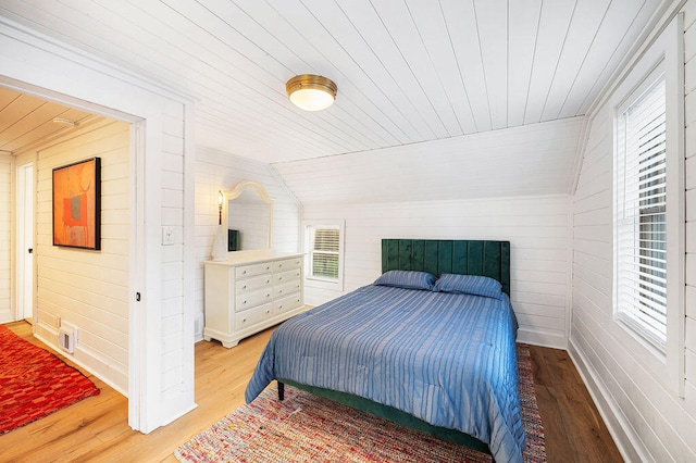 bedroom with wood ceiling, wooden walls, light hardwood / wood-style floors, and lofted ceiling