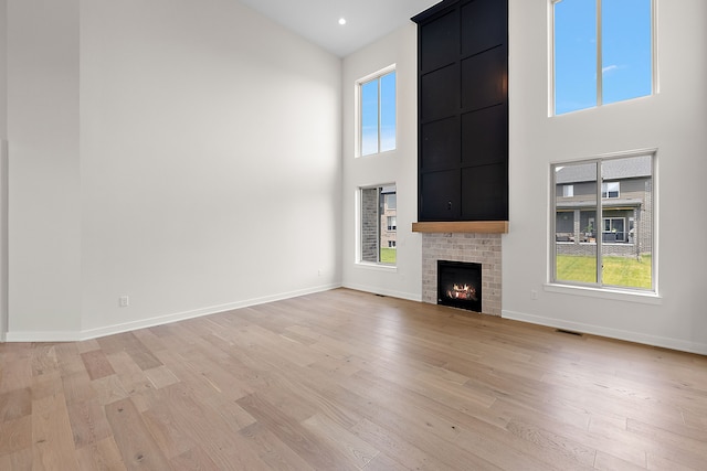 unfurnished living room with a high ceiling, light wood-type flooring, and a brick fireplace