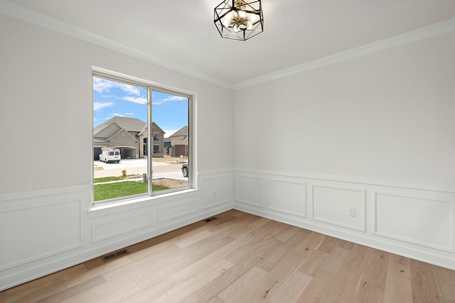 empty room featuring crown molding, light hardwood / wood-style floors, and a notable chandelier