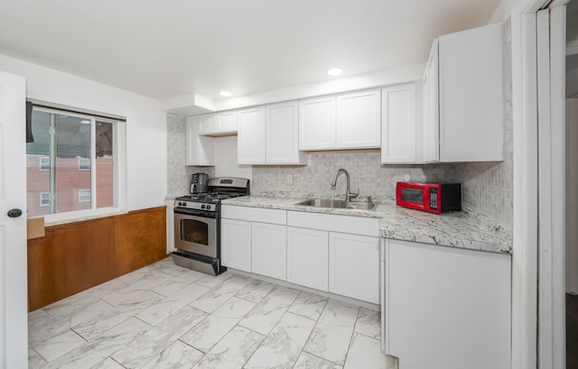 kitchen with tasteful backsplash, light stone counters, stainless steel gas range, sink, and white cabinetry