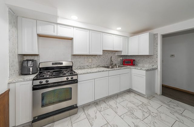 kitchen featuring decorative backsplash, white cabinetry, stainless steel gas range oven, and sink