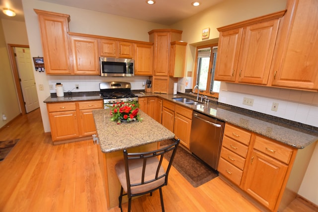 kitchen featuring sink, a center island, stainless steel appliances, dark stone counters, and light hardwood / wood-style floors