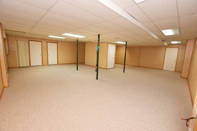 basement featuring light carpet, a paneled ceiling, and wooden walls