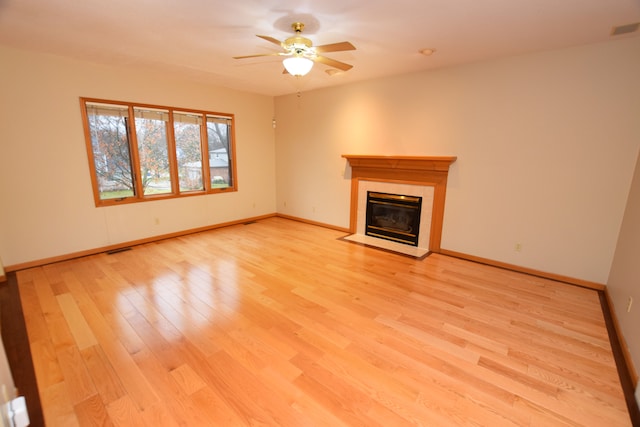 unfurnished living room with a tiled fireplace, ceiling fan, and light hardwood / wood-style flooring