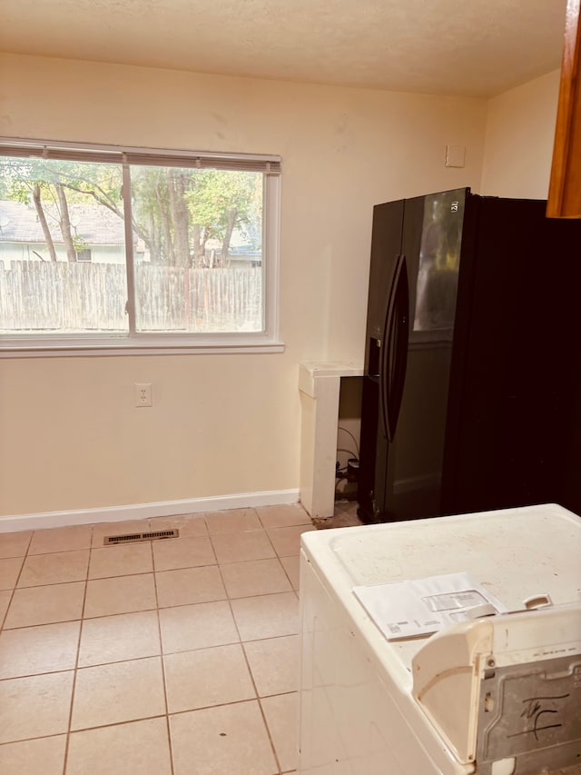 kitchen with black fridge with ice dispenser, a textured ceiling, washer / dryer, and light tile patterned flooring