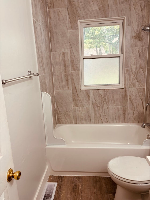 bathroom featuring wood-type flooring, tiled shower / bath combo, and toilet