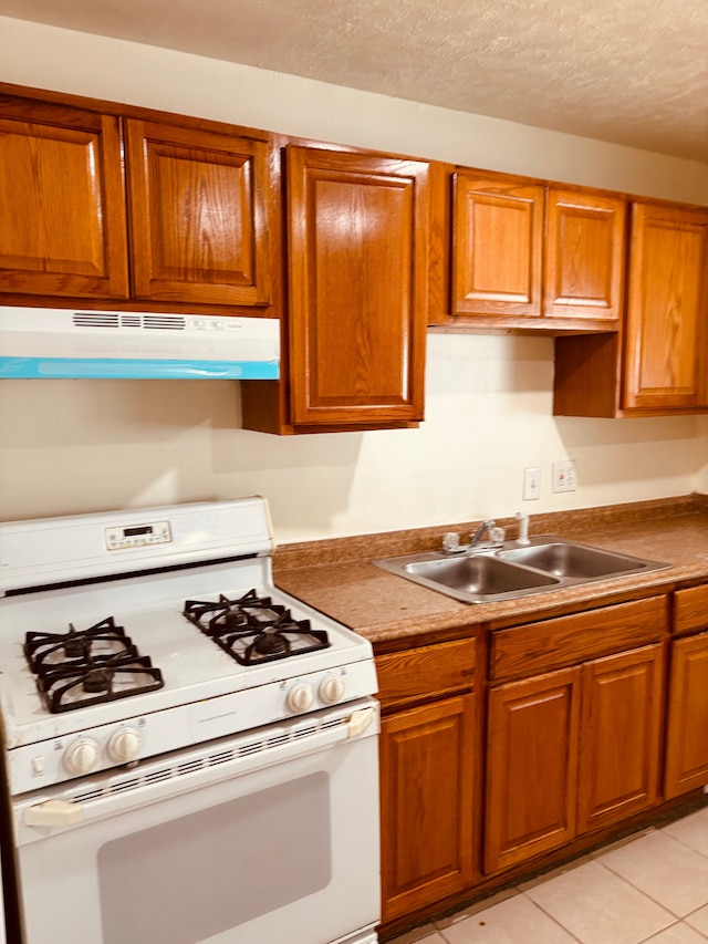 kitchen with light tile patterned floors, a textured ceiling, white gas range, and sink