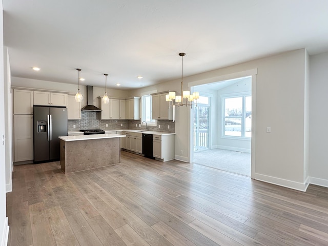 kitchen featuring wall chimney exhaust hood, sink, a center island, hanging light fixtures, and black appliances