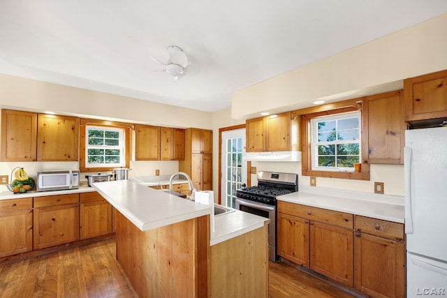 kitchen featuring hardwood / wood-style floors, white appliances, a center island with sink, sink, and ceiling fan