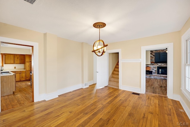 unfurnished dining area featuring sink, a fireplace, a notable chandelier, and light wood-type flooring