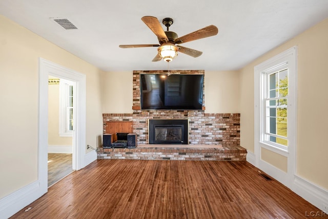 unfurnished living room featuring ceiling fan, wood-type flooring, and a brick fireplace