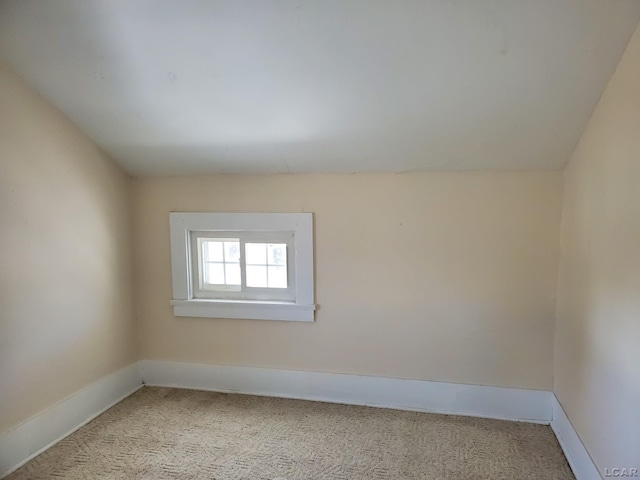 spare room featuring light colored carpet and vaulted ceiling