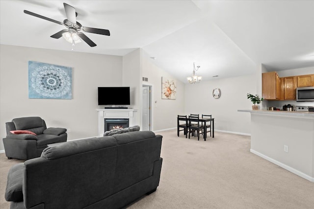 carpeted living room with ceiling fan with notable chandelier and vaulted ceiling