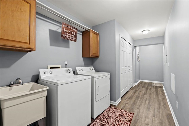 clothes washing area with cabinets, light wood-type flooring, washer and dryer, and sink