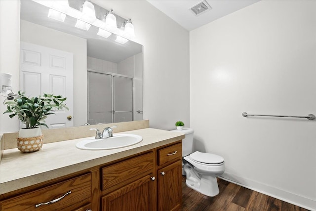 bathroom featuring wood-type flooring, vanity, toilet, and a shower with shower door