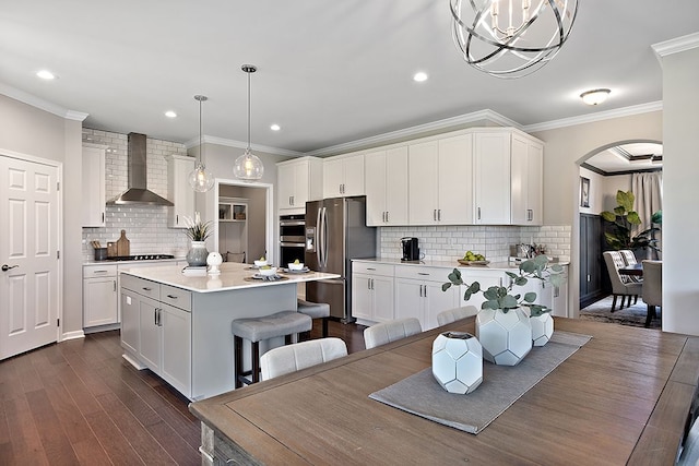 kitchen featuring white cabinets, wall chimney exhaust hood, appliances with stainless steel finishes, decorative light fixtures, and a kitchen island