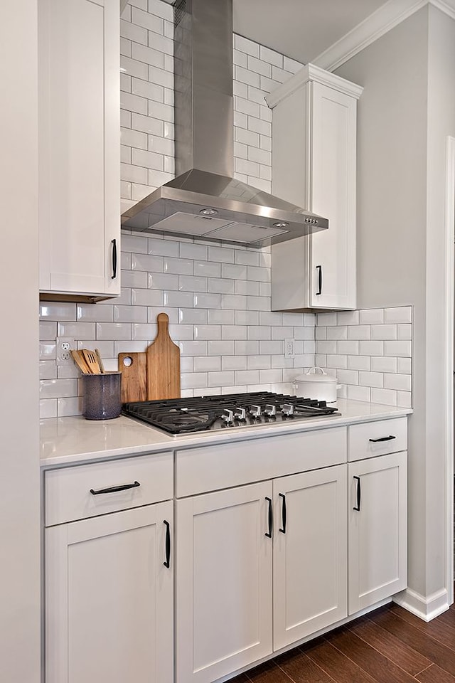 kitchen featuring backsplash, wall chimney range hood, dark hardwood / wood-style flooring, white cabinetry, and stainless steel gas cooktop