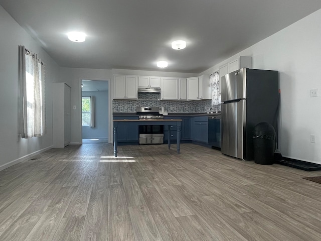 kitchen with white cabinets, blue cabinets, light hardwood / wood-style flooring, decorative backsplash, and appliances with stainless steel finishes