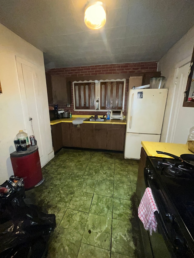 kitchen featuring black range with gas cooktop, dark brown cabinetry, brick wall, and white refrigerator