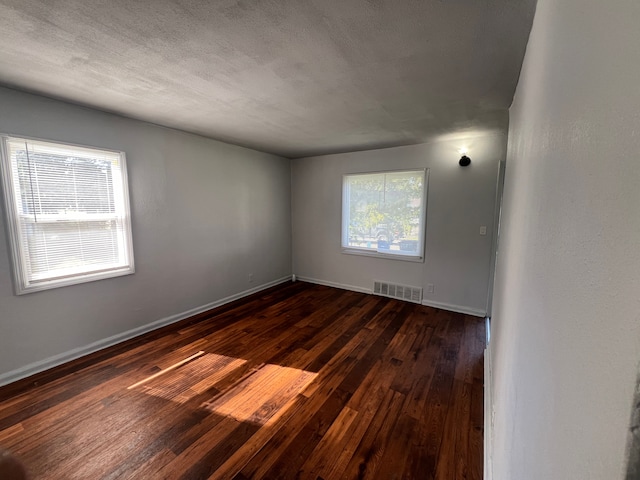 unfurnished room featuring a textured ceiling, dark hardwood / wood-style flooring, and a healthy amount of sunlight