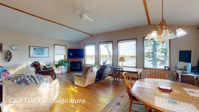 dining area with lofted ceiling, wood finished floors, a fireplace, and ceiling fan with notable chandelier