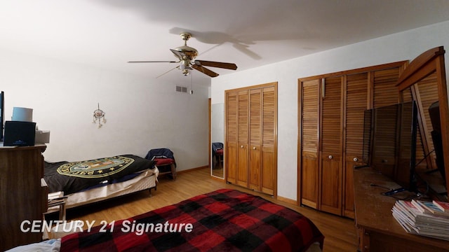 bedroom featuring wood finished floors, visible vents, two closets, and ceiling fan