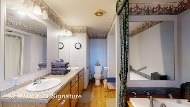 bathroom featuring visible vents, double vanity, a bathing tub, wood finished floors, and a sink