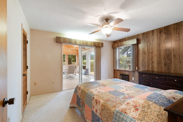 carpeted bedroom with ceiling fan, access to exterior, wood walls, a textured ceiling, and radiator heating unit